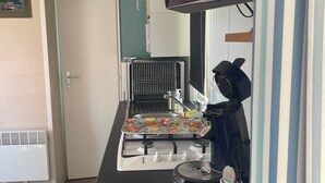 Une petite cuisine équipée d’une cuisinière, d’une machine à café et d’un téléviseur à écran plat fixé au-dessus du comptoir.