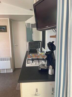 Eine Küchenzeile mit Herd, einer Kaffeemaschine und einem flachbildfernseher, der über der Arbeitsfläche angebracht ist.
