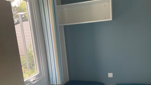 Une chambre avec un lit superposé, une fenêtre avec des rideaux et un radiateur.