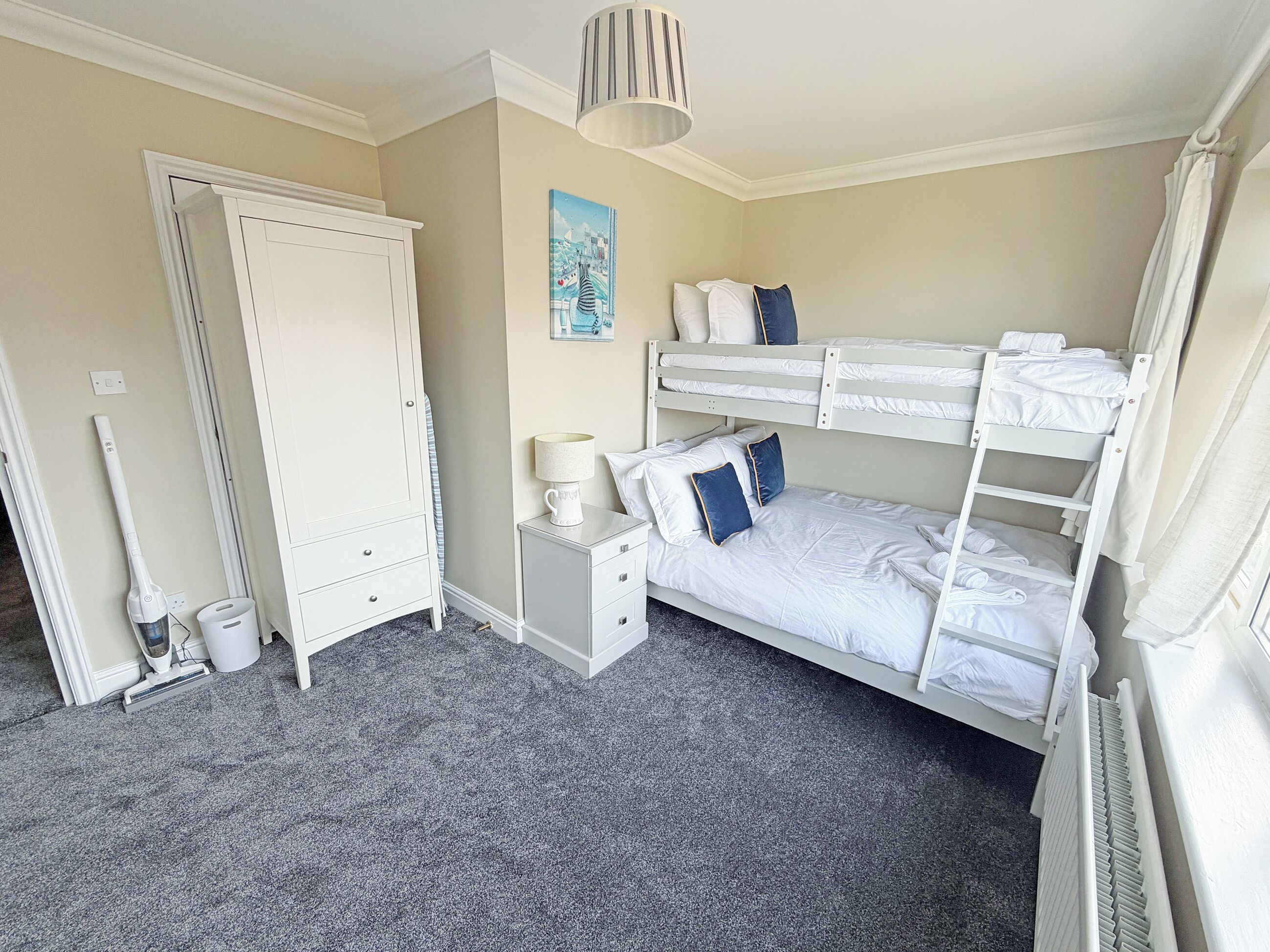 Une chambre avec des lits superposés, une table de chevet, une lampe, un tableau, une armoire et un radiateur.
