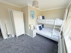 Ein Schlafzimmer mit Etagenbetten, einem Nachttisch, einer Lampe, einem Bild, einem Kleiderschrank und einer Heizung.