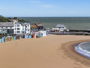 A beach with a row of colorful beach huts, a pier, and buildings along the shore.