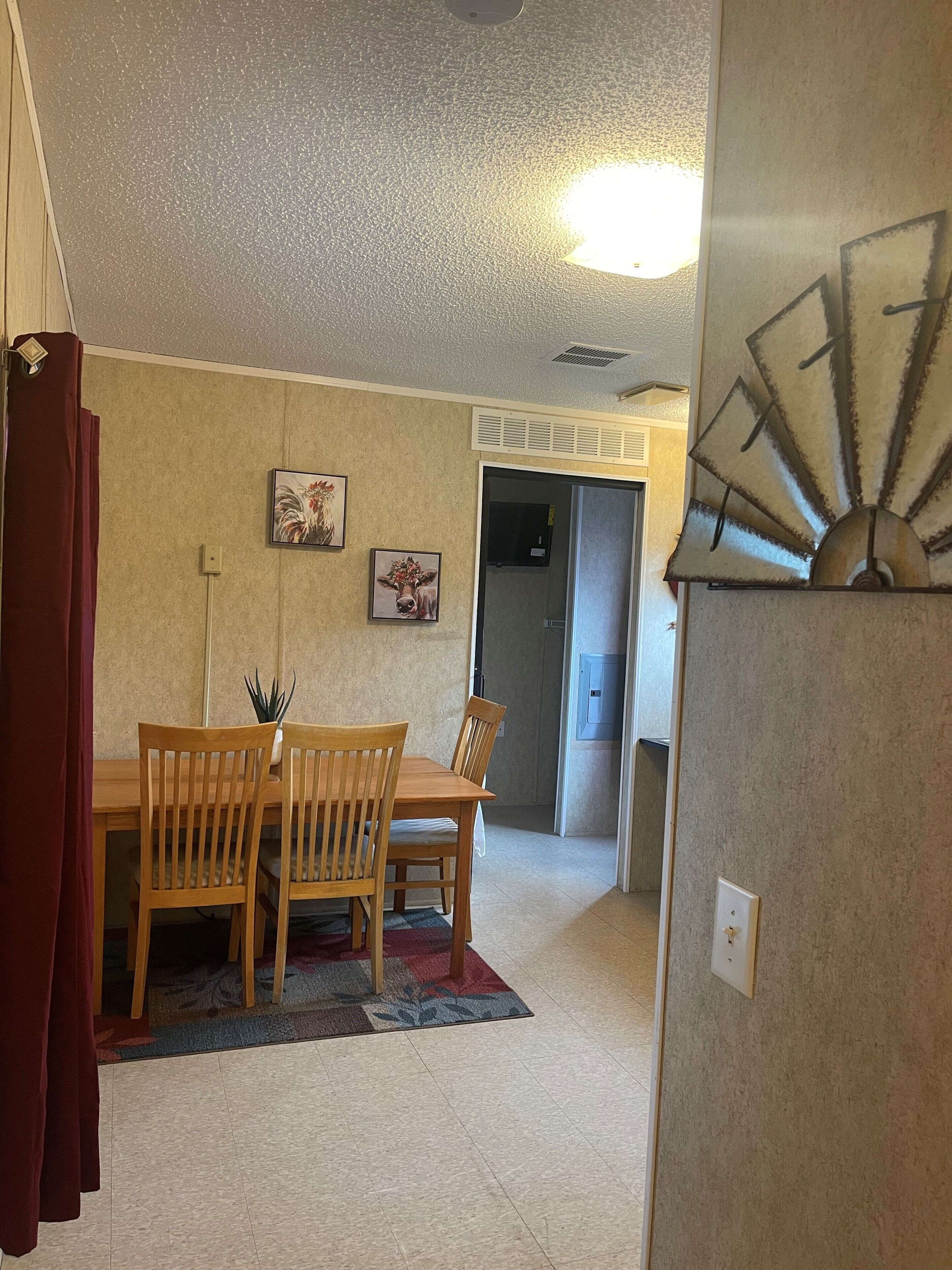 A dining area with a wooden table and chairs, a red curtain, and two wall-mounted pictures.