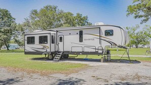 A Sabre Cove RV parked in a campground with a ladder and a small table. - Sugar Valley RV Resort (Van Vleck)
