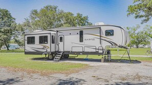 A Sabre Cove RV parked in a campground with a ladder and a small table.