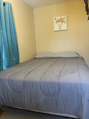 Un dormitorio con cama, un cuadro en la pared y una ventana con cortinas.