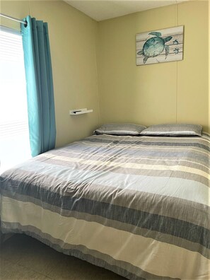 Un dormitorio con una cama, una ventana con cortinas y una obra de arte colgada en la pared.