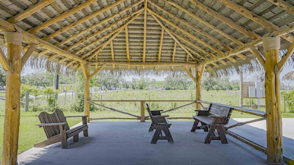 A covered pavilion with a thatched roof, wooden benches, and a concrete floor.