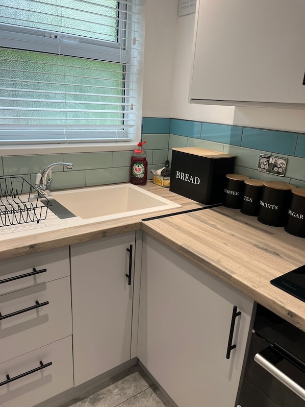 A kitchen with a window, a sink, and storage containers labeled 'BREAD,' 'COFFEE,' 'TEA,' 'SUGAR,' and 'SCOOTIES.'