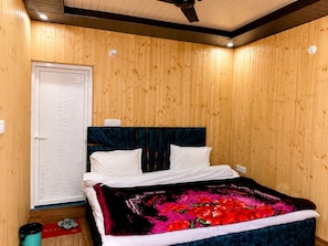 A room with a wooden paneled wall, a bed with a dark headboard, white pillows, and a colorful blanket.