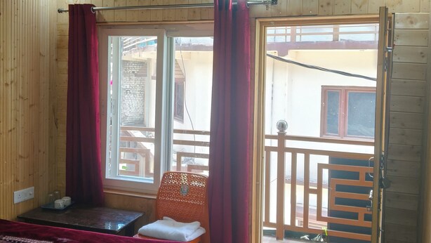 A wooden cabin room with a bed, a table with cups, a chair, and a balcony with a railing. - Yamuna pag pinewood hotel  (Rajgarhi)