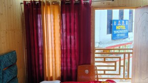 A wooden-paneled room with a bed, curtains, a chair, and a sign for Hotel Yamunakriti Cottages. - Yamuna pag pinewood hotel  (Rajgarhi)