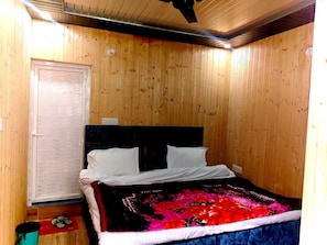 A wooden-paneled room with a bed, a wooden door, and a ceiling fan.