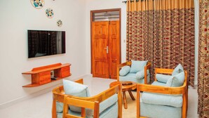 Una sala de estar con muebles de madera, un televisor de pantalla plana, una puerta de madera y cortinas estampadas.