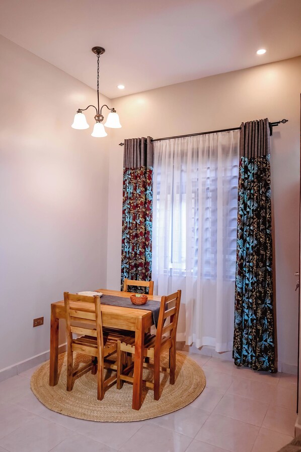 A dining area with a wooden table and chairs, a woven rug, and a ceiling light fixture.