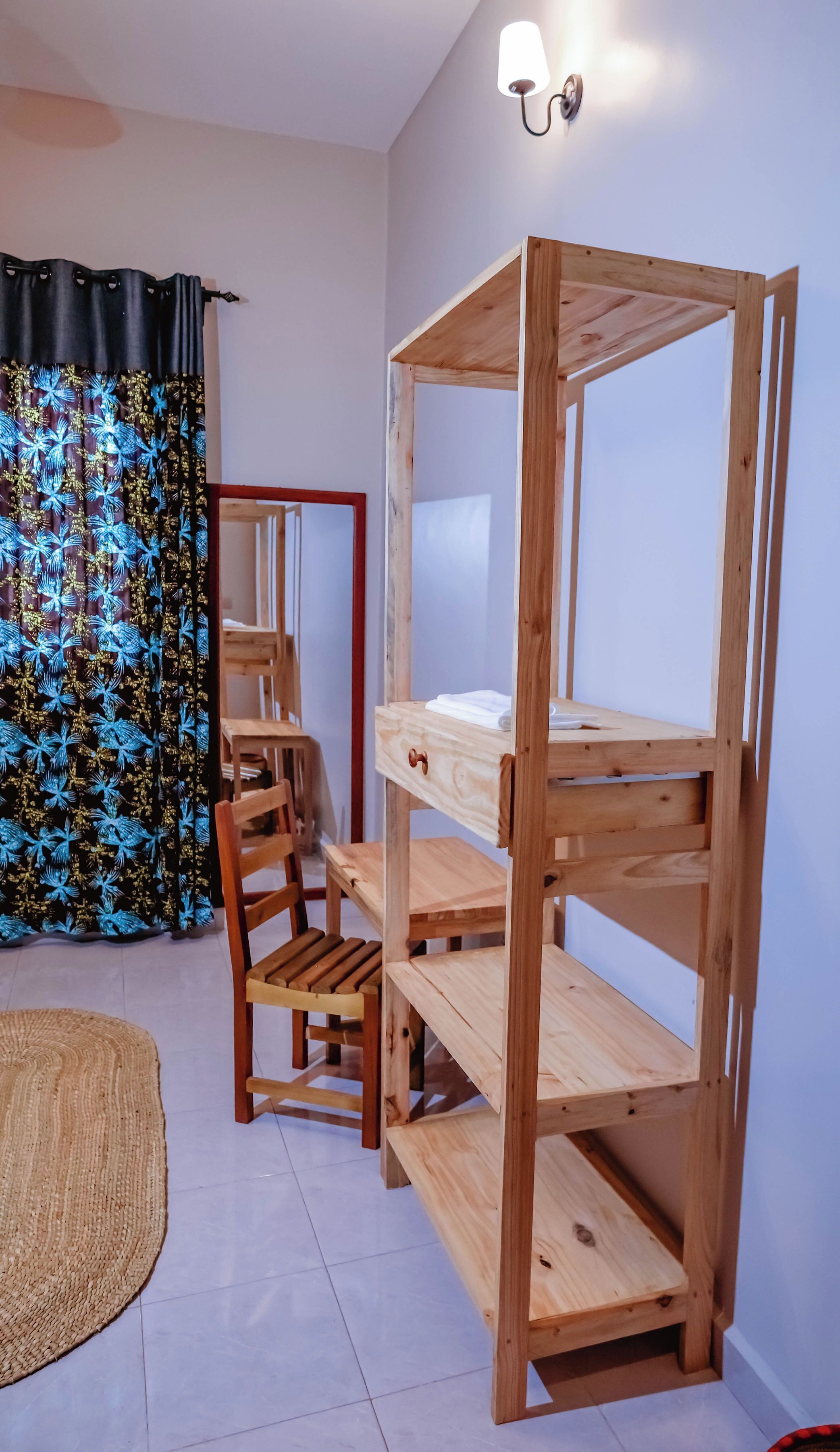 Een stapelbed met houten frame, een stoel en een klein tafeltje in een kamer met betegelde vloer en een raam met gordijnen.