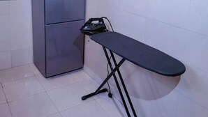 Una cocina compacta con refrigerador, tabla de planchar y un armario de madera.