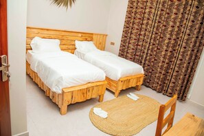 Een kamer met twee houten bedden, een geweven mat en een gordijn met patroon.