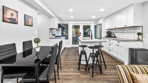 A modern kitchen with white cabinets, a dining area with black chairs, and a striped sofa.