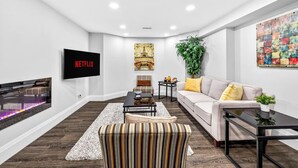 A modern living room with a flat-screen TV, a fireplace, a sofa, a striped ottoman, and a coffee table.