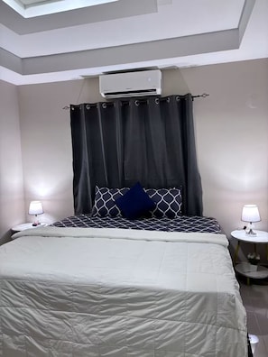 Una camera da letto con un letto, una finestra, un condizionatore d'aria e due comodini con lampade.