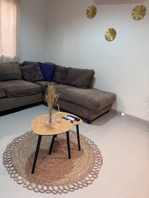 Un soggiorno con divano, tavolino rotondo con base intrecciata e decorazioni a parete.