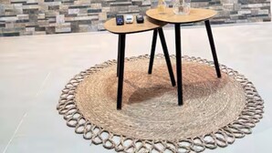Un soggiorno moderno con parete effetto pietra, una TV a schermo piatto montata sopra un tavolo rotondo in legno con due sedie e un tappeto intrecciato sul pavimento.