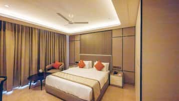 Quarto de hotel moderno com uma cama grande, uma escrivaninha, uma cadeira, uma mesa de cabeceira e um ventilador de teto.