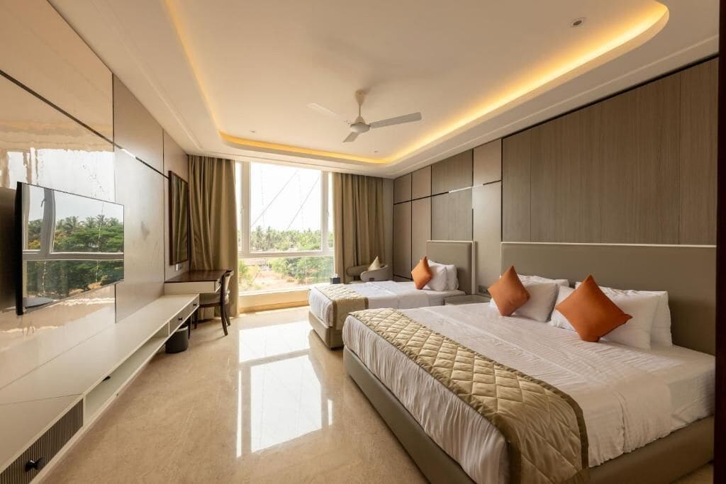 Habitación de hotel con dos camas, televisor, ventilador de techo y una ventana grande.