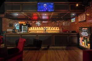 A bar area with a television mounted on the wall, a Budweiser sign, and a variety of bottles and glasses on the counter.
