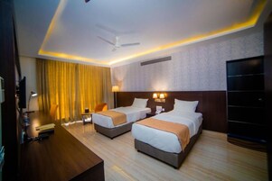 Habitación de hotel con dos camas, un escritorio, un televisor y un ventilador de techo.