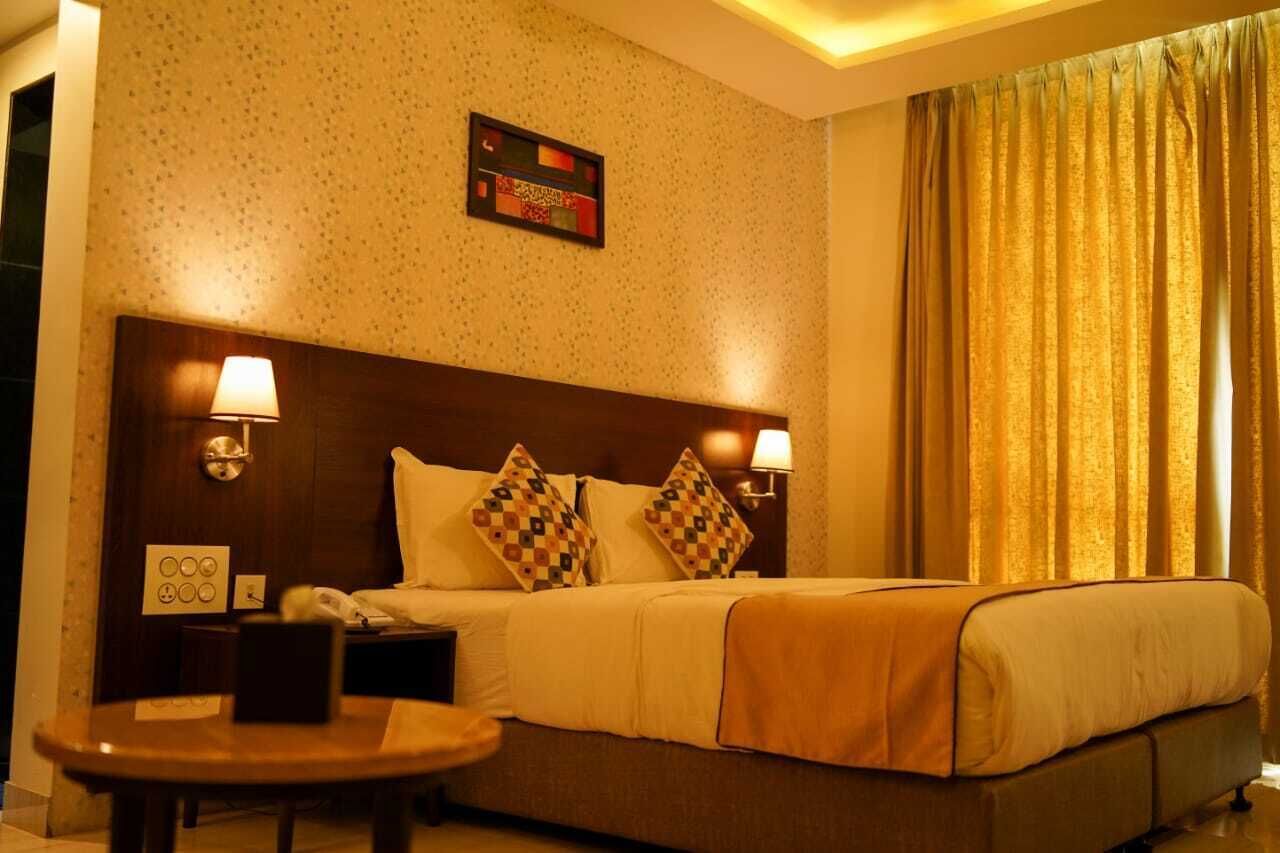 Une chambre d’hôtel avec un grand lit, deux lampes de chevet, une petite table et une œuvre d’art accrochée au mur.