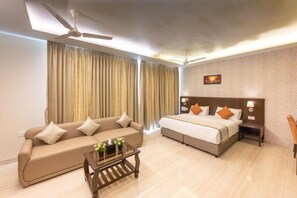 A modern hotel room with a sofa, a bed, a ceiling fan, and a painting on the wall. - Fortune Plaza hotel (Varambally)