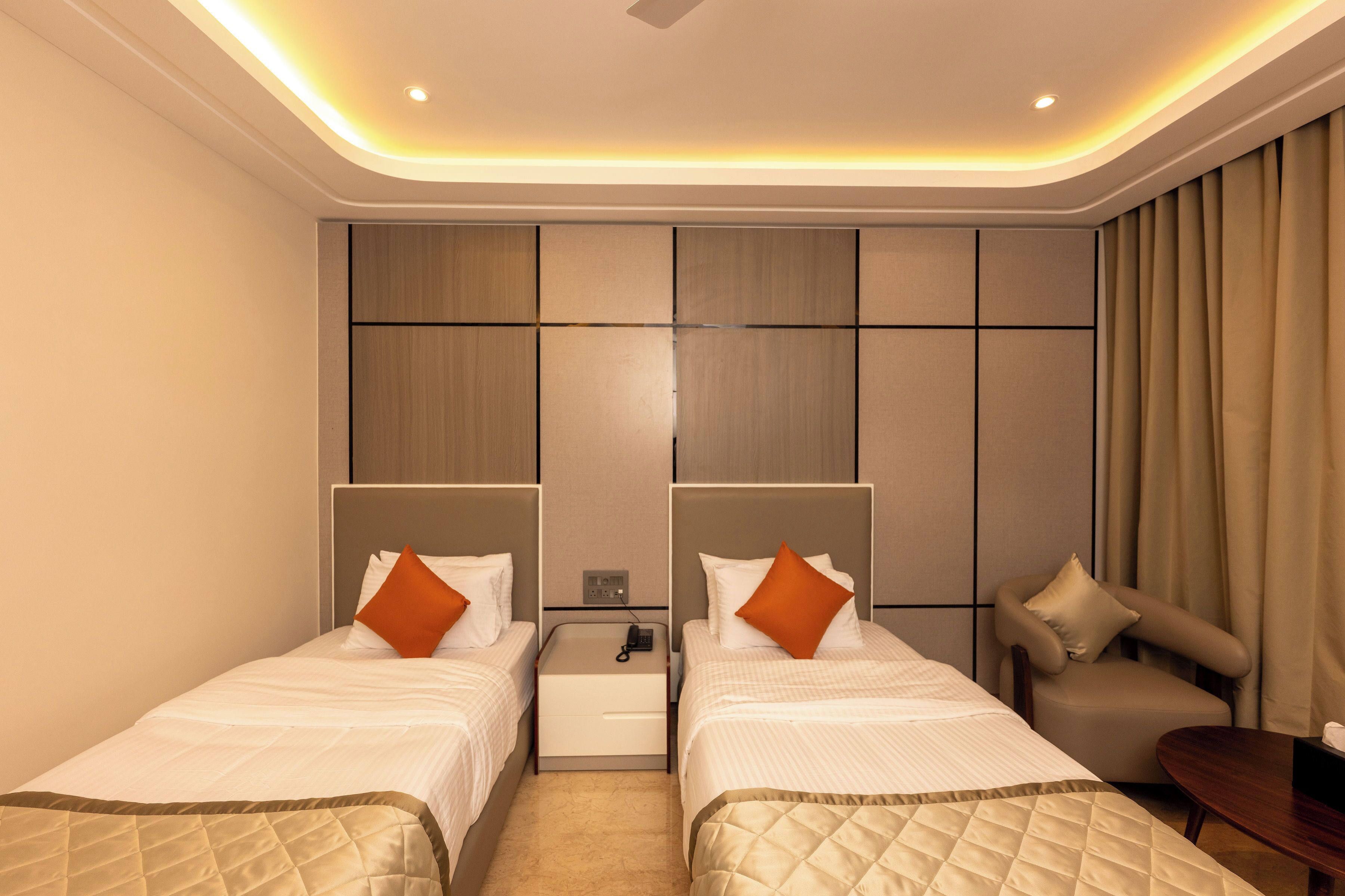 Habitación de hotel con dos camas, una mesita, un sofá y una mesita de noche con un teléfono.
