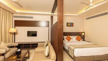 A hotel room with a bed, a sofa, a TV, a ceiling fan, and a window.