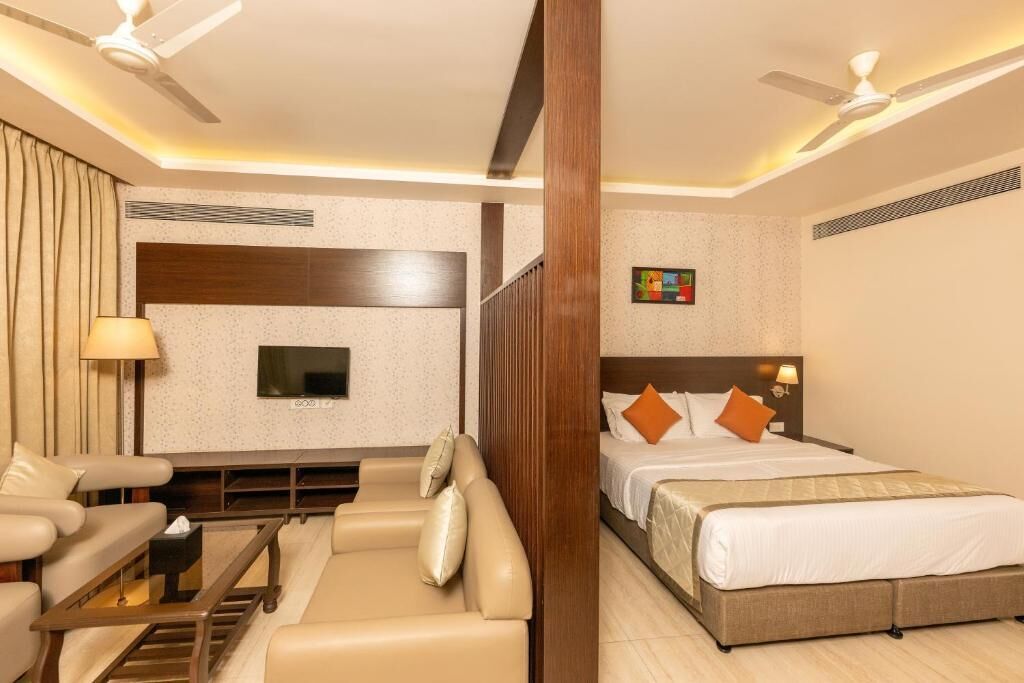 A hotel room with a bed, a sofa, a TV, and a ceiling fan.