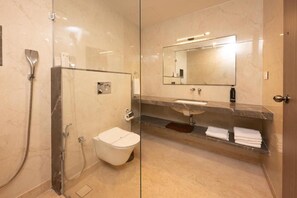 A modern bathroom with a glass-enclosed shower, a toilet, a sink with a marble countertop, and a mirror above the sink. - Fortune Plaza hotel (Varambally)