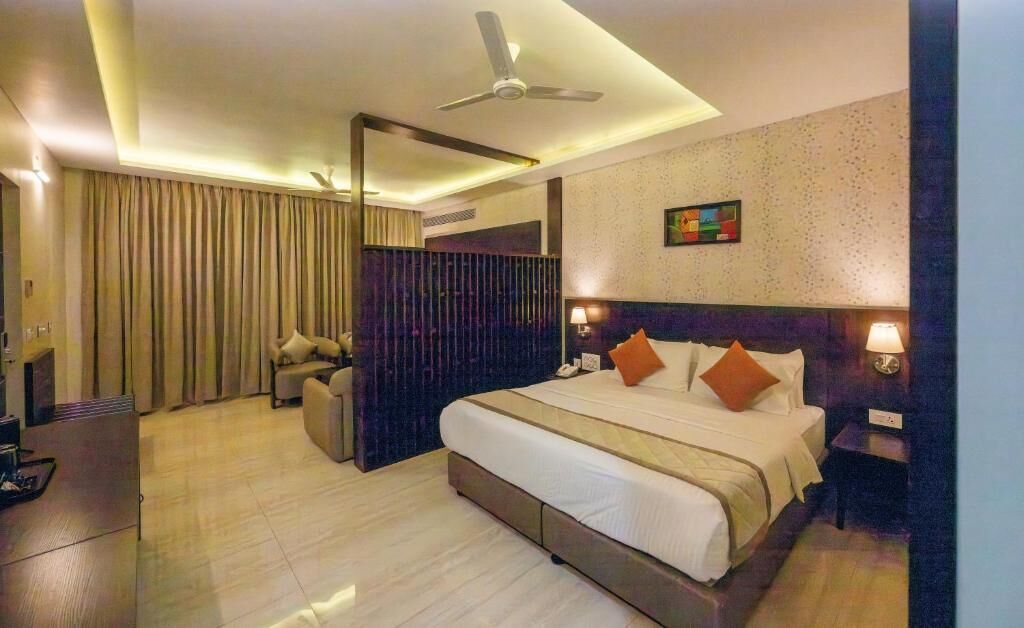 Une chambre d’hôtel comprenant un lit, des lampes de chevet, un bureau, une chaise, un ventilateur de plafond et un grand miroir.