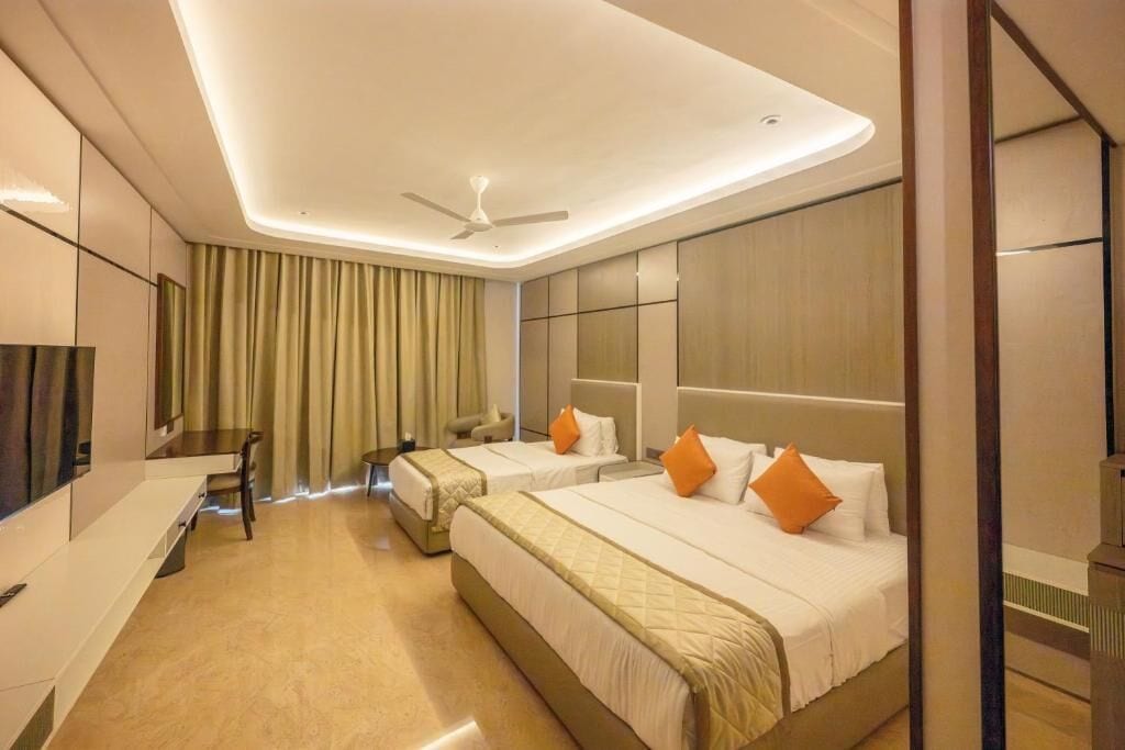 Ein Hotelzimmer mit zwei Betten, einem Schreibtisch, einem Sessel, einem Fernseher und einem Deckenventilator.
