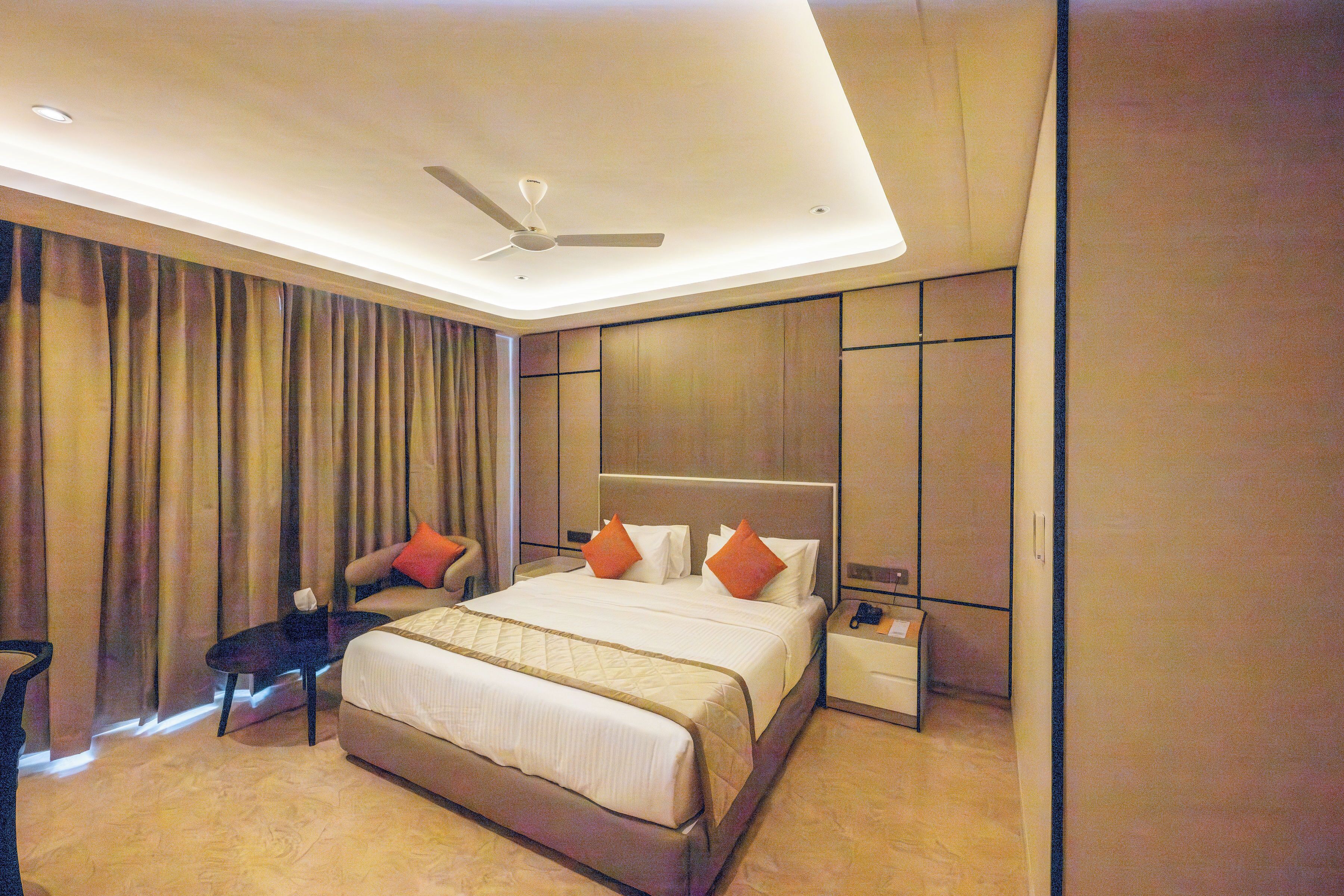 Habitación de hotel con cama, mesita de noche, silla, escritorio y ventilador de techo.
