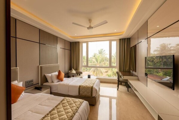A hotel room with two beds, a TV, a ceiling fan, and a large window with a view of palm trees. - Fortune Plaza hotel (Varambally)