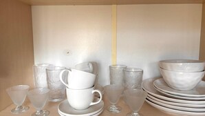 Valikoima valkoisia keramiikka-astioita, kuten kuppeja, kulhoja ja lautasia, on aseteltu esille puupinnalla.