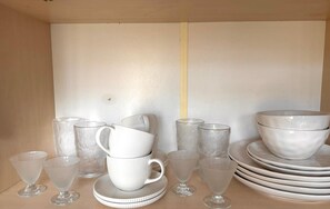 A collection of white ceramic tableware including cups, bowls, and plates arranged on a wooden surface. - Narva Promenade (Narva)