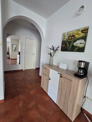 A hallway with a kitchen area, a coffee maker, and a painting on the wall. - The Breathtaking Views - Kotorscapes II (Muo)
