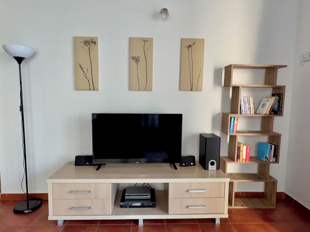 A living room with a TV, speakers, a bookshelf, and artwork on the wall.