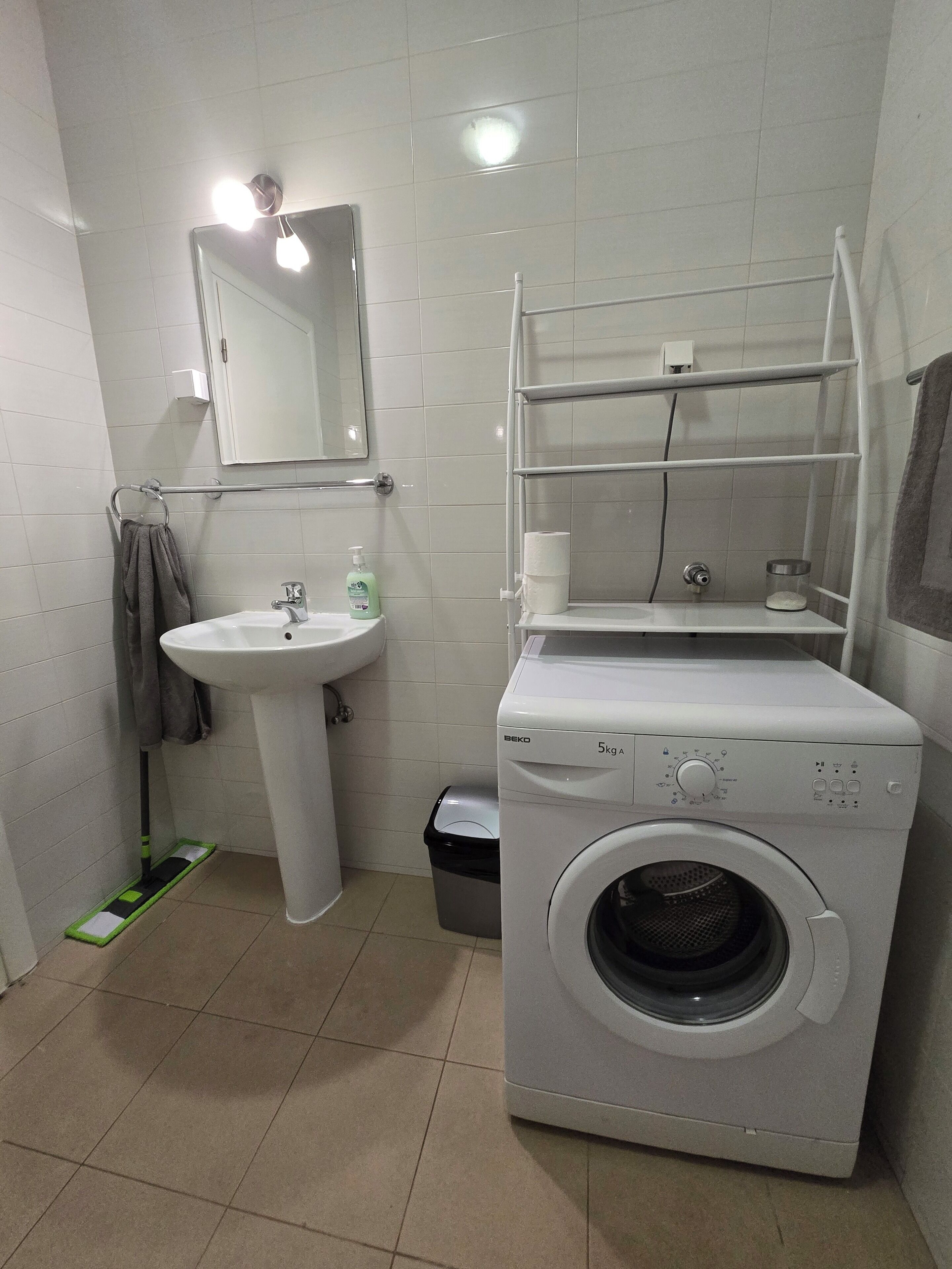 Ein kleines Badezimmer mit Waschbecken, Spiegel, Handtuchhalter und einer Frontlader-Waschmaschine.