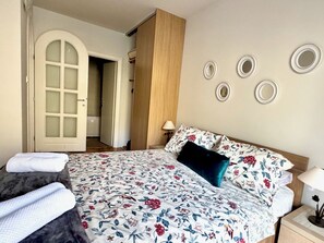 A bedroom with a bed, a nightstand, a lamp, a door, and a wall with circular decorations. - The Breathtaking Views - Kotorscapes II (Muo)