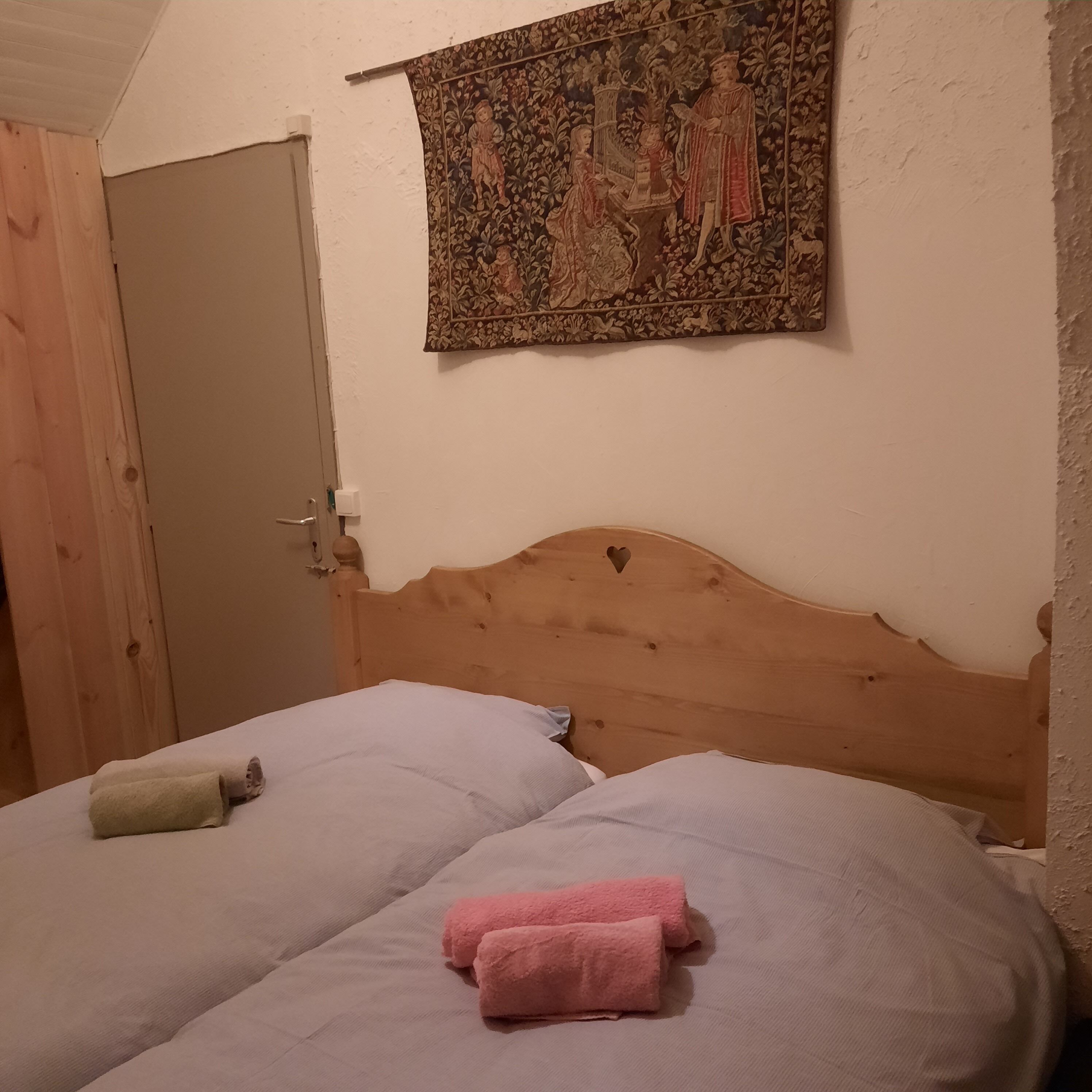 A bedroom with two beds, a wooden headboard, a tapestry on the wall, and a door.