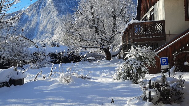 Schneebedeckte Landschaft mit einem Berg im Hintergrund, ein Holzhaus mit Balkon und ein Parkschild.
