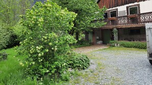Ein rustikales Holzhaus mit Balkon, umgeben von üppiger Vegetation und Bergen im Hintergrund.